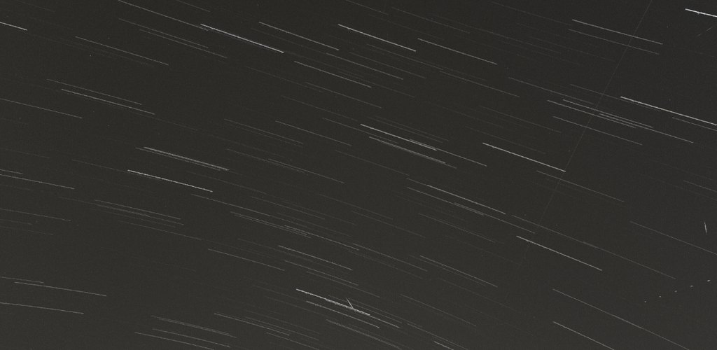 Star trails: hundreds of short parallel white arcs across a dark grey sky, with a few plane or satellite streaks crossing them
